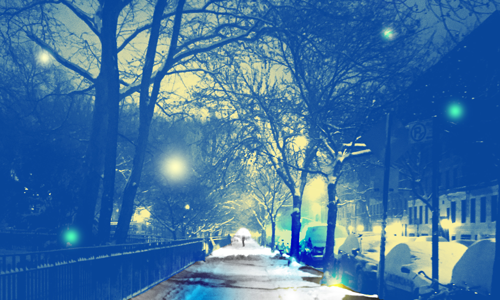 A snowy, blue city sidewalk stretches forward, with trees and street lights on either side.